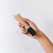 Hand holding a tube of BB Cream foundation against a white background