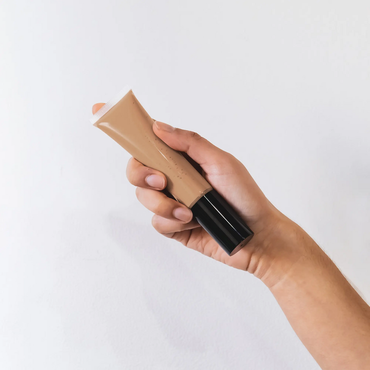 Hand holding a tube of BB Cream foundation against a white background