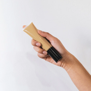 Hand holding a tube of foundation against a white background