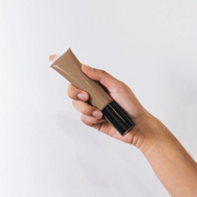 Hand holding a tube of BB Cream brown cream on a white background