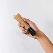 Hand holding a tube of BB Cream foundation against a white background